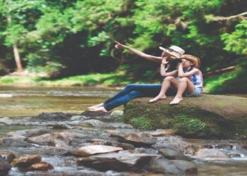 mother and daughter using binoculars on mountain stream rocks